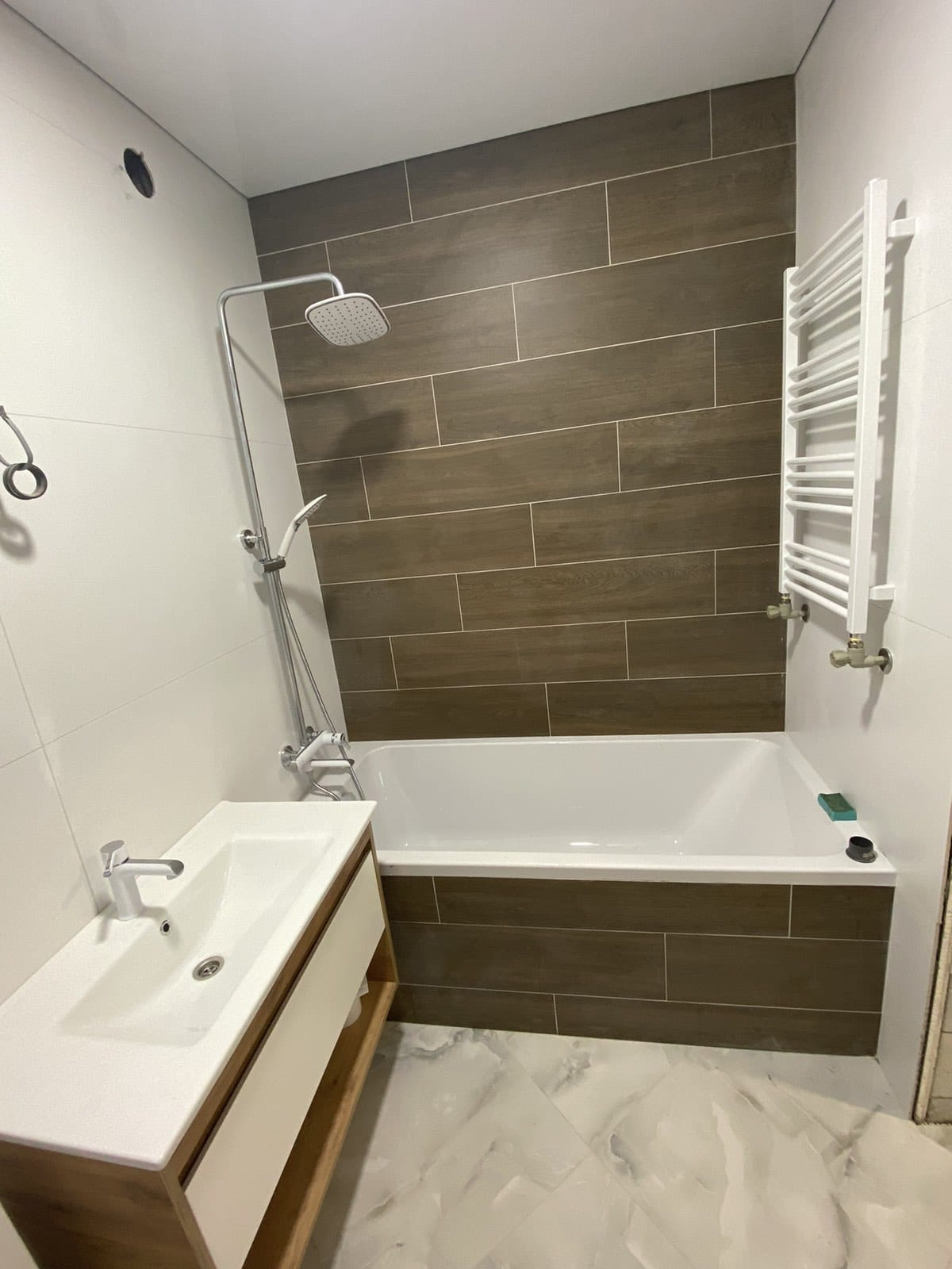 Badezimmer mit Wanne, Holzoptik-Fliesen, Regendusche und Waschtisch mit Holzfront