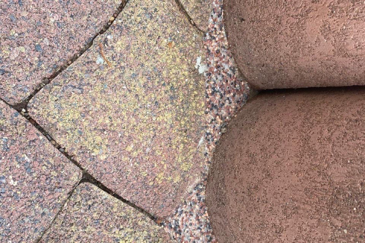 Nahaufnahme einer Pflasterfuge: Betonsteinpflaster in Rosé und Ocker trifft auf einen rotbraunen Randstein